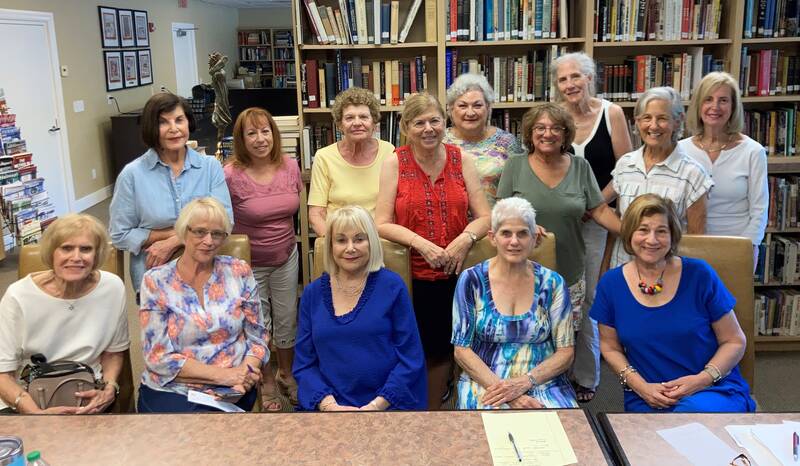 14 sisterhood board members pose at a table in the library
