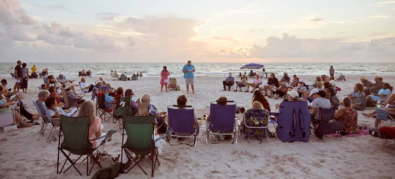 Members gather in a semi-circle on the beach at sunset. Rabbi Miller and Cantor Azu face the group with the sunset at their backs.