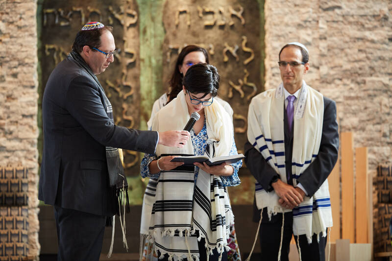 Bat Mitzvah reads a prayer on the bimah while Rabbi Miller holds the microphone and parents look on.
